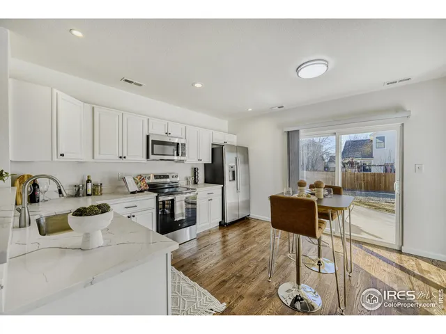 a kitchen with stainless steel appliances kitchen island granite countertop a refrigerator a stove a sink and white cabinets with wooden floor