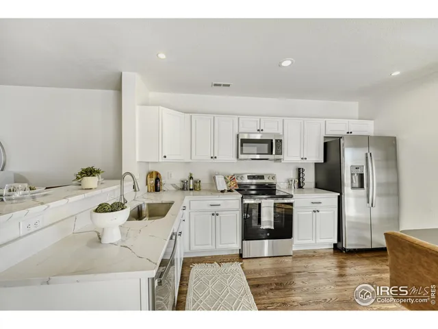 a kitchen with stainless steel appliances kitchen island granite countertop a refrigerator a stove a sink and white cabinets with wooden floor