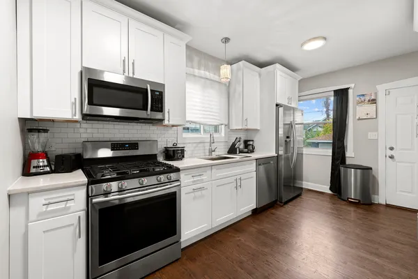 a kitchen with stainless steel appliances white cabinets a sink a stove a microwave and wooden floors