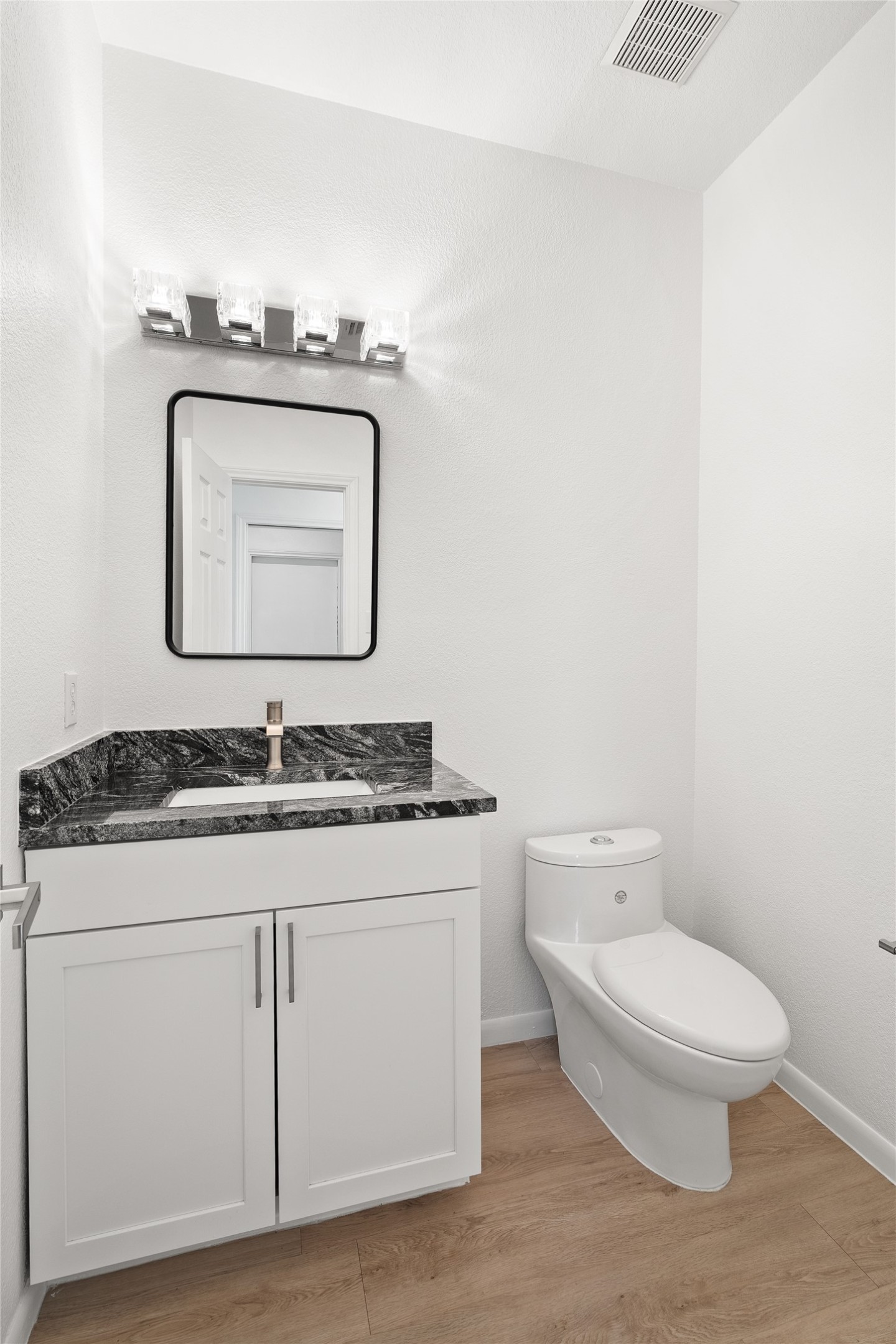 206 River Down Road Georgetown, TX 78628 - Photo 20 of 39 Bathroom featuring wood-finish flooring, a white vanity with shaker-style cabinetry, a dark patterned countertop, an undermount sink, and a modern single-handle faucet