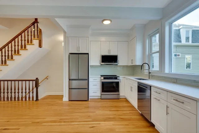 a kitchen with stainless steel appliances granite countertop a refrigerator a stove top oven a sink dishwasher and white cabinets with wooden floor