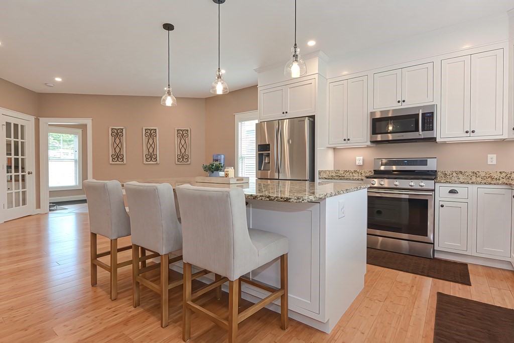 128 Nourse Road Bolton, MA 01740 - Photo 10 of 42 a kitchen with stainless steel appliances granite countertop a stove a refrigerator a kitchen island a dining table and chairs with wooden floor