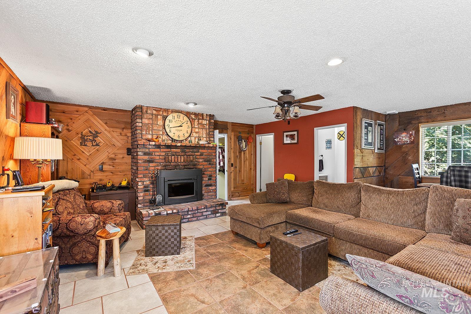25314 Soldiers Meadow Road Winchester, ID 83555 - Photo 8 of 45 Living room featuring wooden walls, a textured ceiling, a ceiling fan, and a brick fireplace