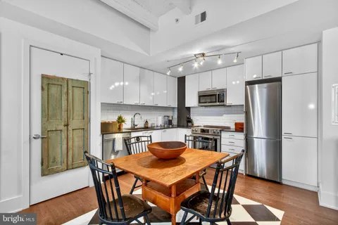 a kitchen with stainless steel appliances a dining table a refrigerator a stove a dining table and chairs