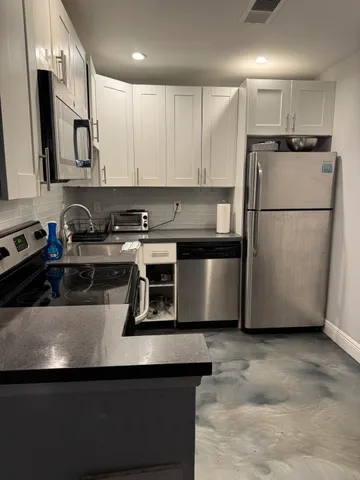 a kitchen with stainless steel appliances granite countertop a sink a stove a refrigerator a microwave and white cabinets