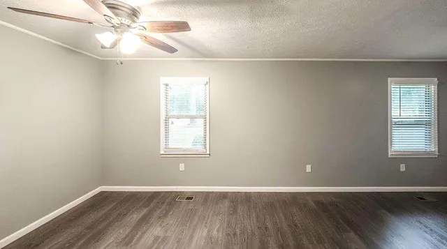 an empty room with wooden floor fan and windows