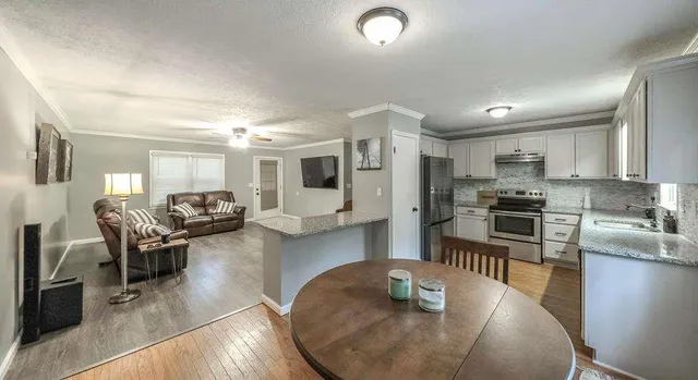 a kitchen with stainless steel appliances granite countertop a stove top oven a sink a dining table and chairs with wooden floor