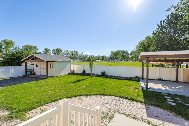 5525 Hampton Way Stansbury Park, UT 84074 - Photo 31 of 35 Expansive backyard featuring a manicured lawn, a detached storage shed with an overhang, a covered patio area, and a white privacy fence bordering a large open field