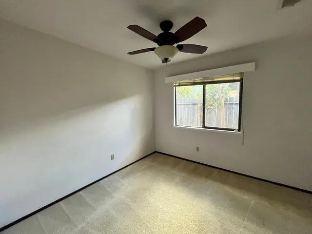 an empty room with ceiling fan and windows