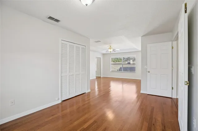 an empty room with wooden floor fan and windows
