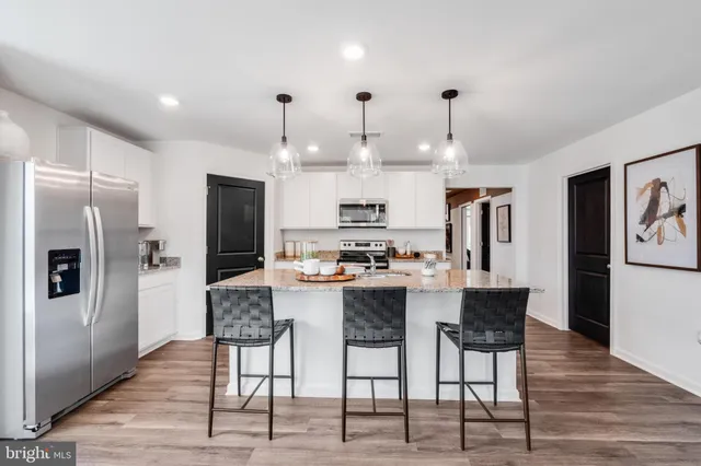 a kitchen with stainless steel appliances kitchen island granite countertop a refrigerator a stove a microwave oven a sink with island and chairs with wooden floor