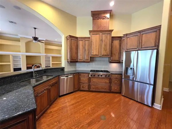 a kitchen with stainless steel appliances granite countertop a refrigerator a sink dishwasher a stove with wooden cabinets and floor