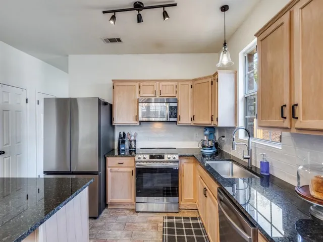 a kitchen with granite countertop a refrigerator a sink a stove and cabinets