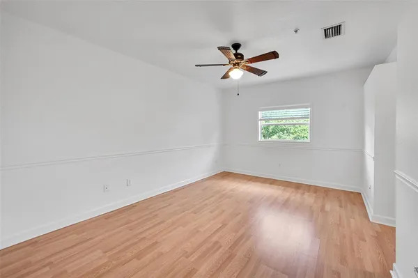 an empty room with wooden floor fan and windows
