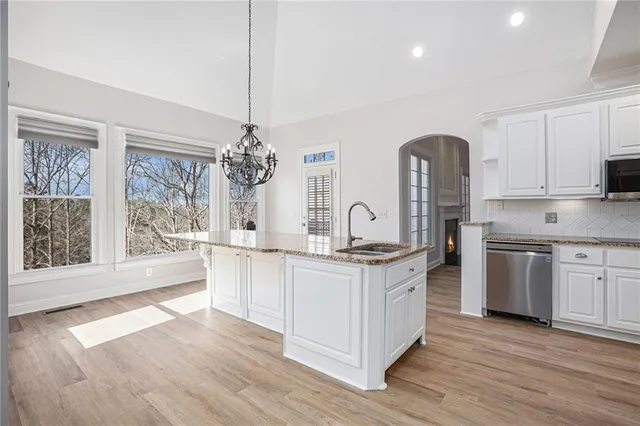 a kitchen with stainless steel appliances granite countertop a stove a sink dishwasher a refrigerator and white cabinets with wooden floor