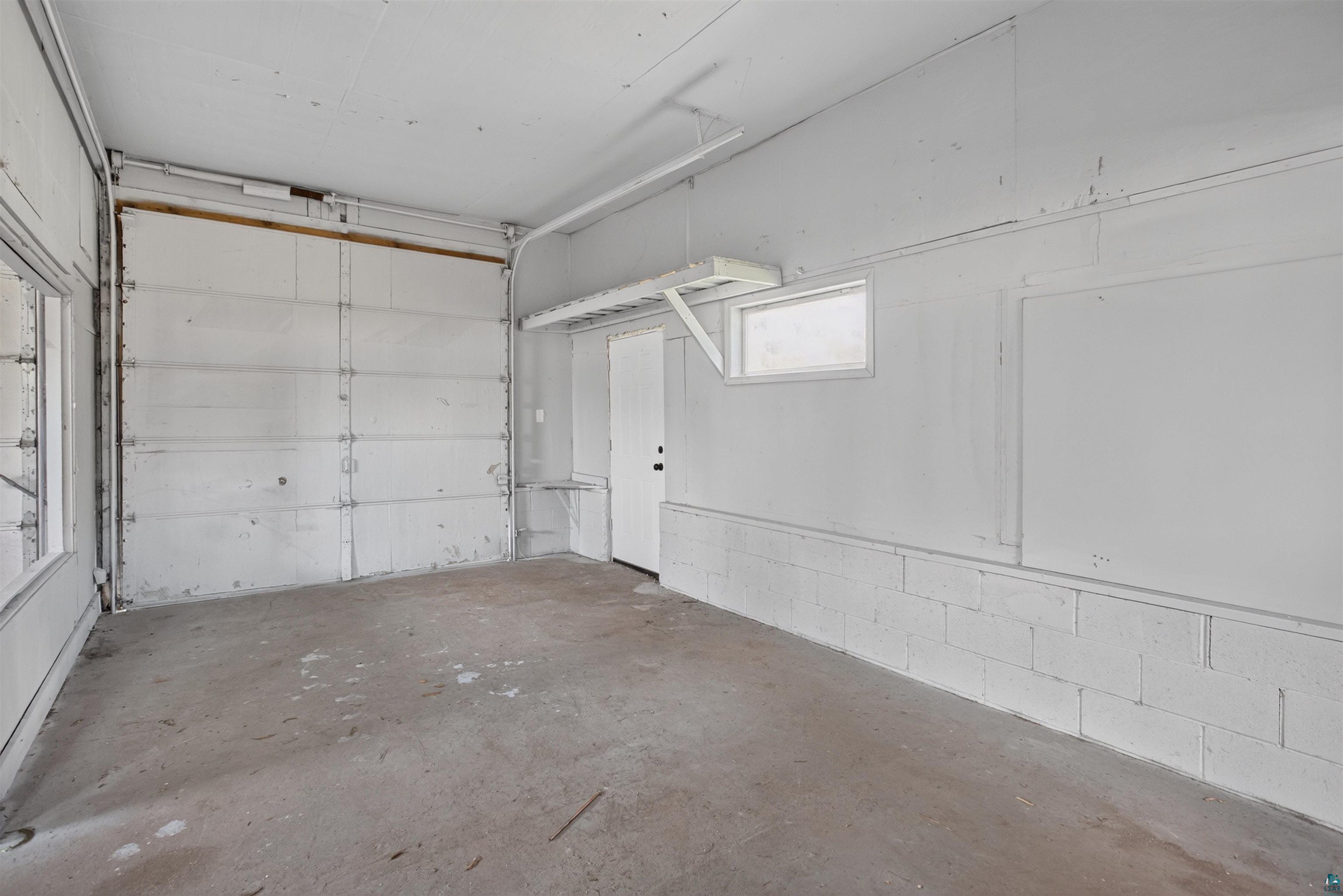 5868 Rice Lake Road Duluth, MN 55803 - Photo 31 of 39 Concrete flooring garage with an overhead door, white painted walls, and a side entry door