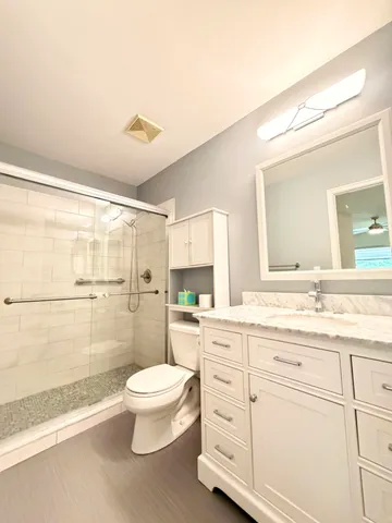 a bathroom with a granite countertop sink a toilet a mirror and shower