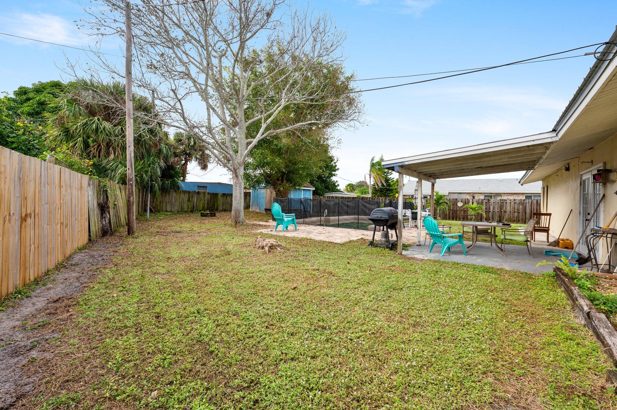 822 Onyx Drive Northeast Palm Bay, FL 32905 - Photo 16 of 21 a view of a backyard with table and chairs under an umbrella with wooden fence