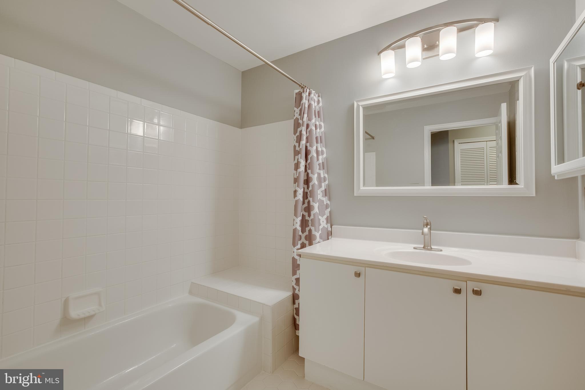 20575 Snowshoe Square, Unit 302 Ashburn, VA 20147 - Photo 17 of 32 a bathroom with a bathtub sink vanity and mirror