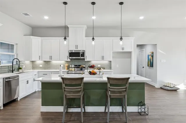 a kitchen with stainless steel appliances kitchen island granite countertop a table chairs refrigerator and sink