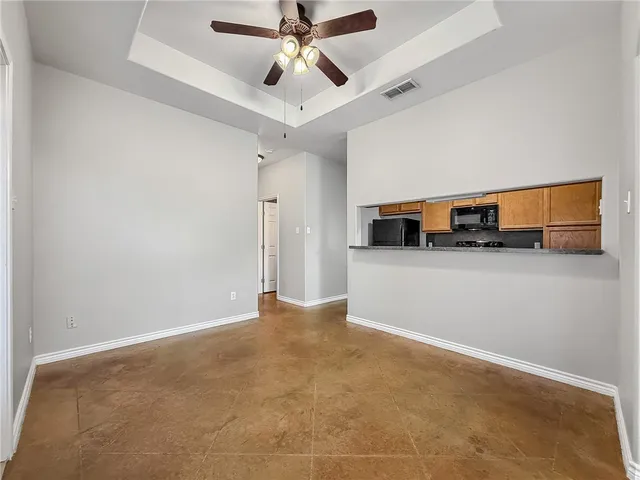 a view of a livingroom with kitchen appliances and a ceiling fan