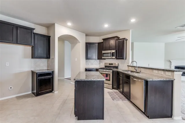 a kitchen with stainless steel appliances granite countertop a stove top oven a sink dishwasher a refrigerator and a oven with wooden floor