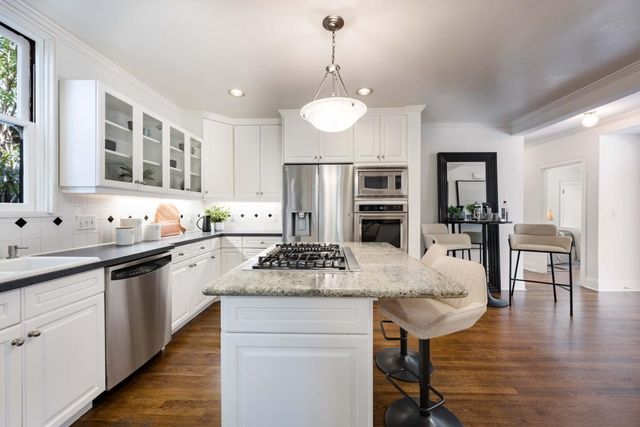 a kitchen with stainless steel appliances granite countertop a stove a refrigerator a sink a dining table and chairs with wooden floor