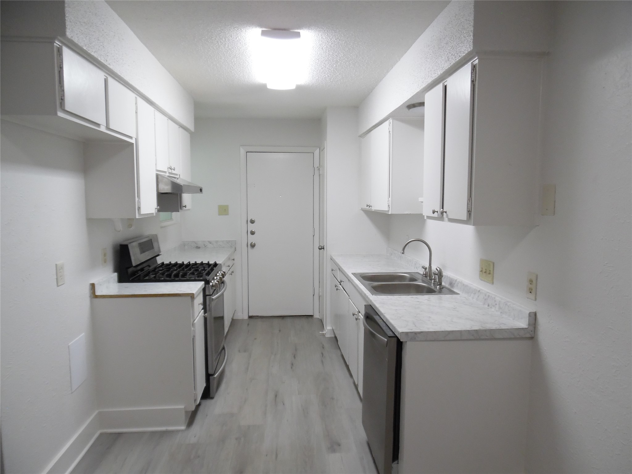 7400 Dixie Drive, Unit B Austin, TX 78744 - Photo 6 of 15 Galley kitchen featuring white cabinetry, wood-finish flooring, stainless steel gas range, stainless steel dishwasher, and a double basin stainless steel sink