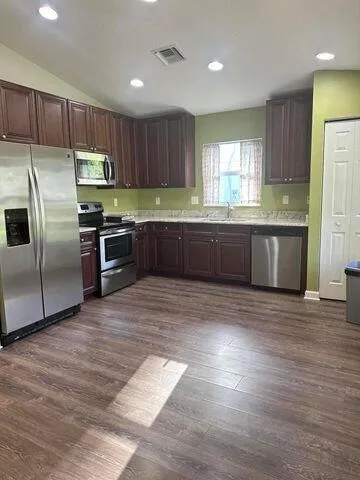 a large kitchen with granite countertop a stove a sink dishwasher a refrigerator and a microwave oven with wooden floor