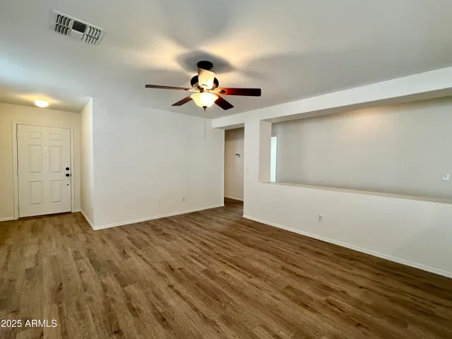 a view of an empty room with chandelier fan and wooden floor