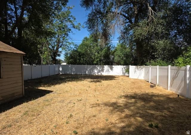 3161 Adams Avenue Ogden, UT 84403 - Photo 14 of 17 Expansive yard featuring a white privacy fence, mature trees, and a detached shed with wood siding and a shingle roof