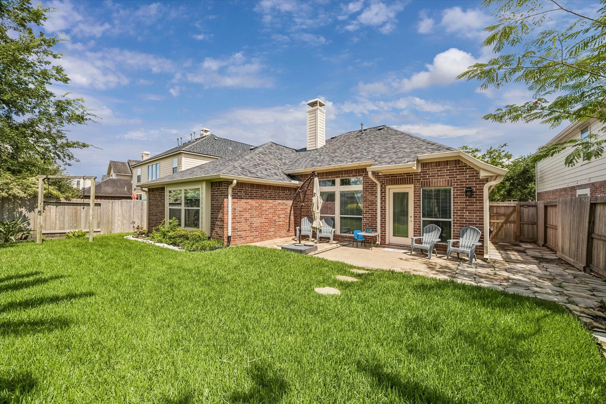 3118 Valley Court Manvel, TX 77578 - Photo 32 of 38 This photo showcases a charming backyard with a well-maintained lawn, a brick exterior, and a patio area perfect for relaxing or entertaining. The space is fenced for privacy, and mature trees provide shade and a welcoming atmosphere.
