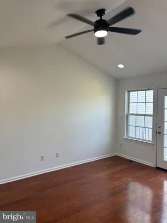 an empty room with wooden floor ceiling fan and windows