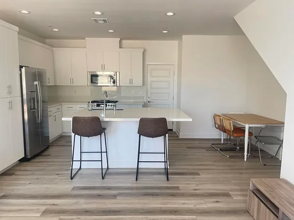 a kitchen with stainless steel appliances kitchen island granite countertop a dining table chairs and a refrigerator