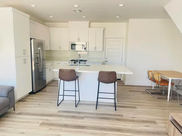 a kitchen with stainless steel appliances kitchen island granite countertop a dining table chairs and a refrigerator