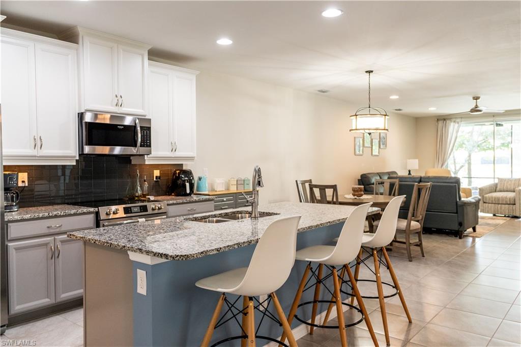 14888 Edgewater Circle Naples, FL 34114 - Photo 11 of 33 a kitchen with stainless steel appliances granite countertop a stove a sink a microwave a dining table and chairs