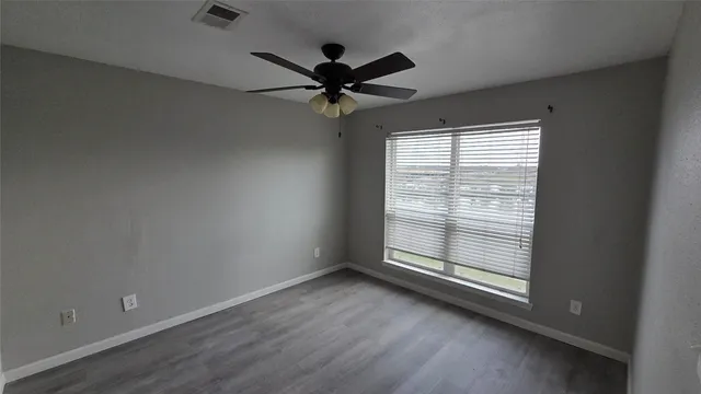 an empty room with wooden floor fan and windows