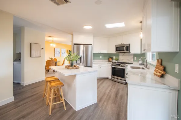 a kitchen with stainless steel appliances a stove top oven a sink a refrigerator white cabinets and wooden floor