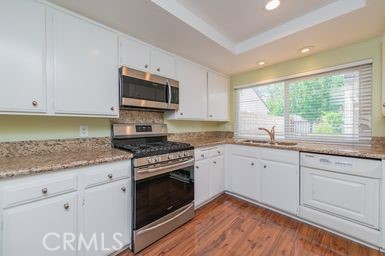 14 Featherwood Irvine, CA 92612 - Photo 16 of 32 a kitchen with granite countertop a stove a sink dishwasher and white cabinets with wooden floor
