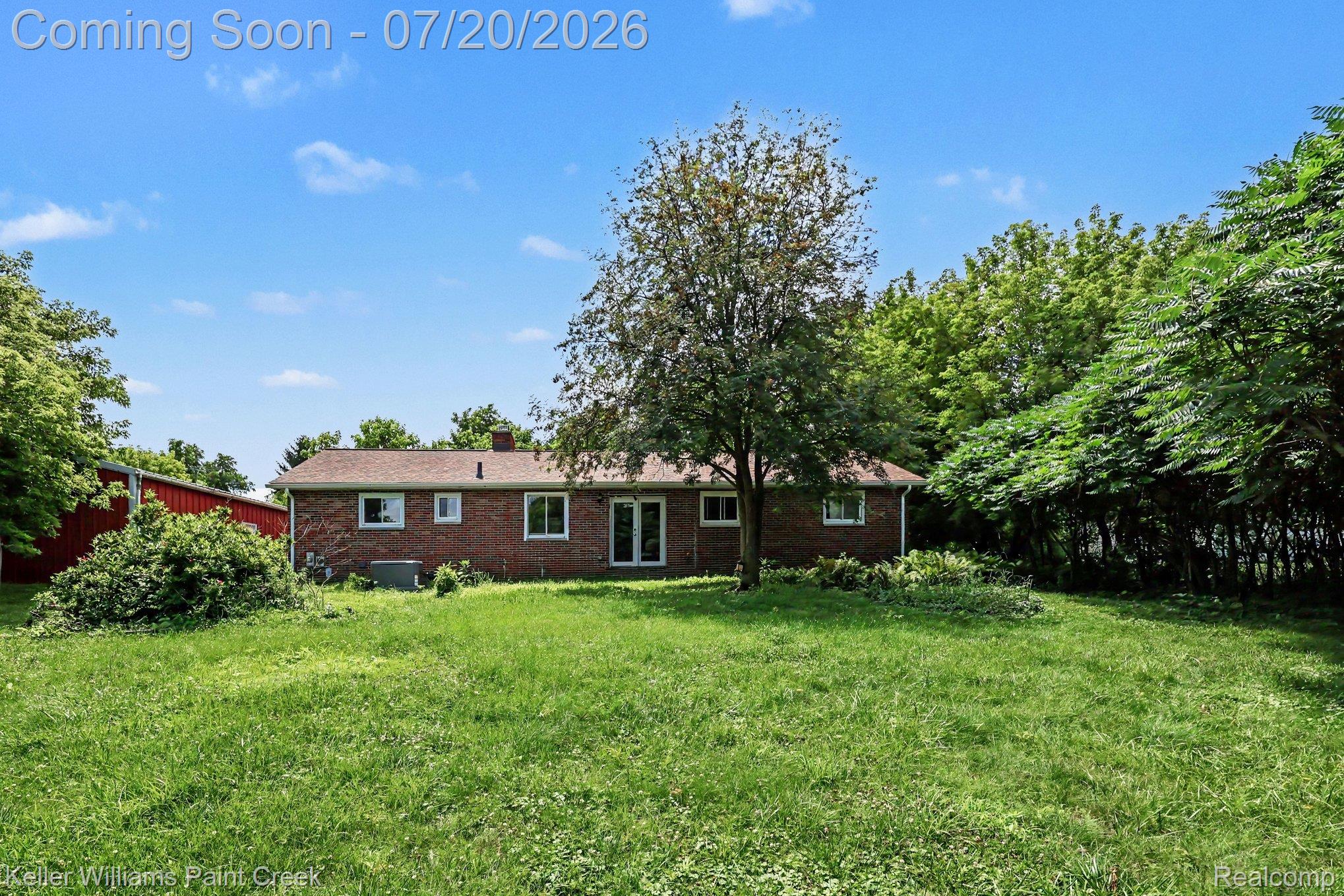 1371 East Leonard Road Leonard, MI 48367 - Photo 25 of 32 Expansive rear yard featuring a brick-clad home with a brown shingle roof, mature trees, and a detached red outbuilding