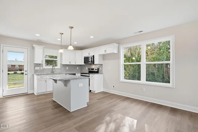 a kitchen with stainless steel appliances granite countertop a refrigerator a sink dishwasher a stove and white countertops with wooden floor