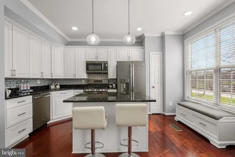 a kitchen with stainless steel appliances granite countertop a stove a sink a microwave a refrigerator and white cabinets with wooden floor