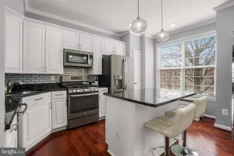 a kitchen with stainless steel appliances granite countertop a stove top oven a sink dishwasher a dining table and chairs with wooden floor