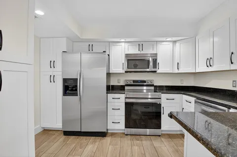 a kitchen with stainless steel appliances white cabinets a sink a stove a refrigerator and microwave