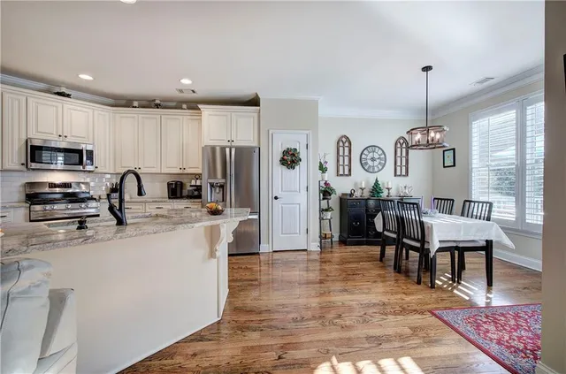 a kitchen with stainless steel appliances granite countertop a refrigerator a stove a sink a dining table and chairs with wooden floor