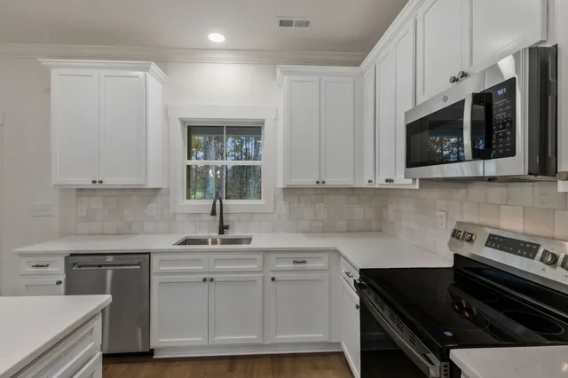a kitchen with white cabinets a sink stove and microwave