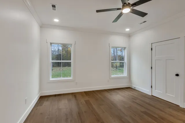 an empty room with wooden floor fan and windows