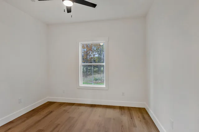 an empty room with wooden floor chandelier fan and windows