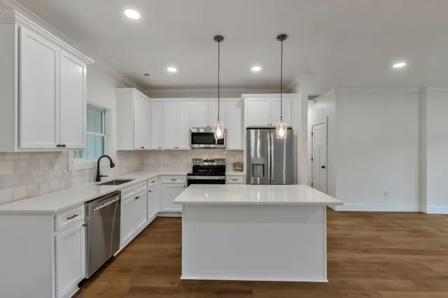 a kitchen with stainless steel appliances granite countertop a stove a sink a refrigerator and white cabinets with wooden floor