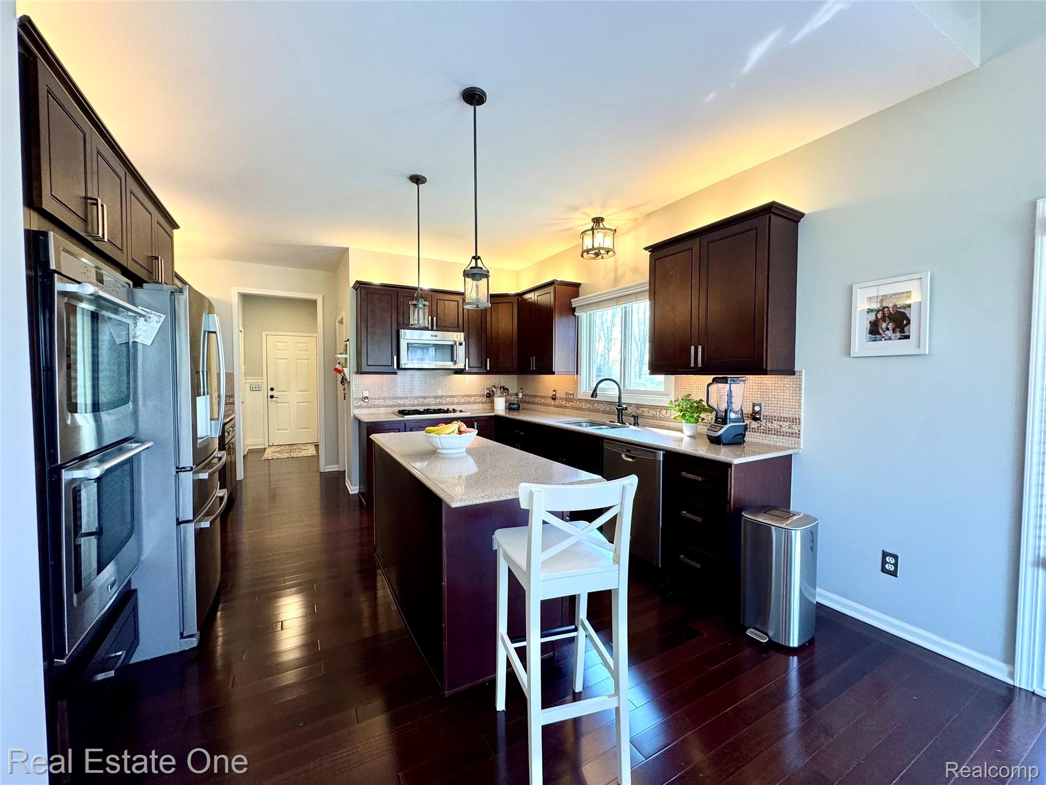 419 Roundview Drive Rochester, MI 48307 - Photo 10 of 29 Kitchen featuring dark wood finish cabinetry, a center island, light stone countertops, stainless steel appliances, and pendant lighting